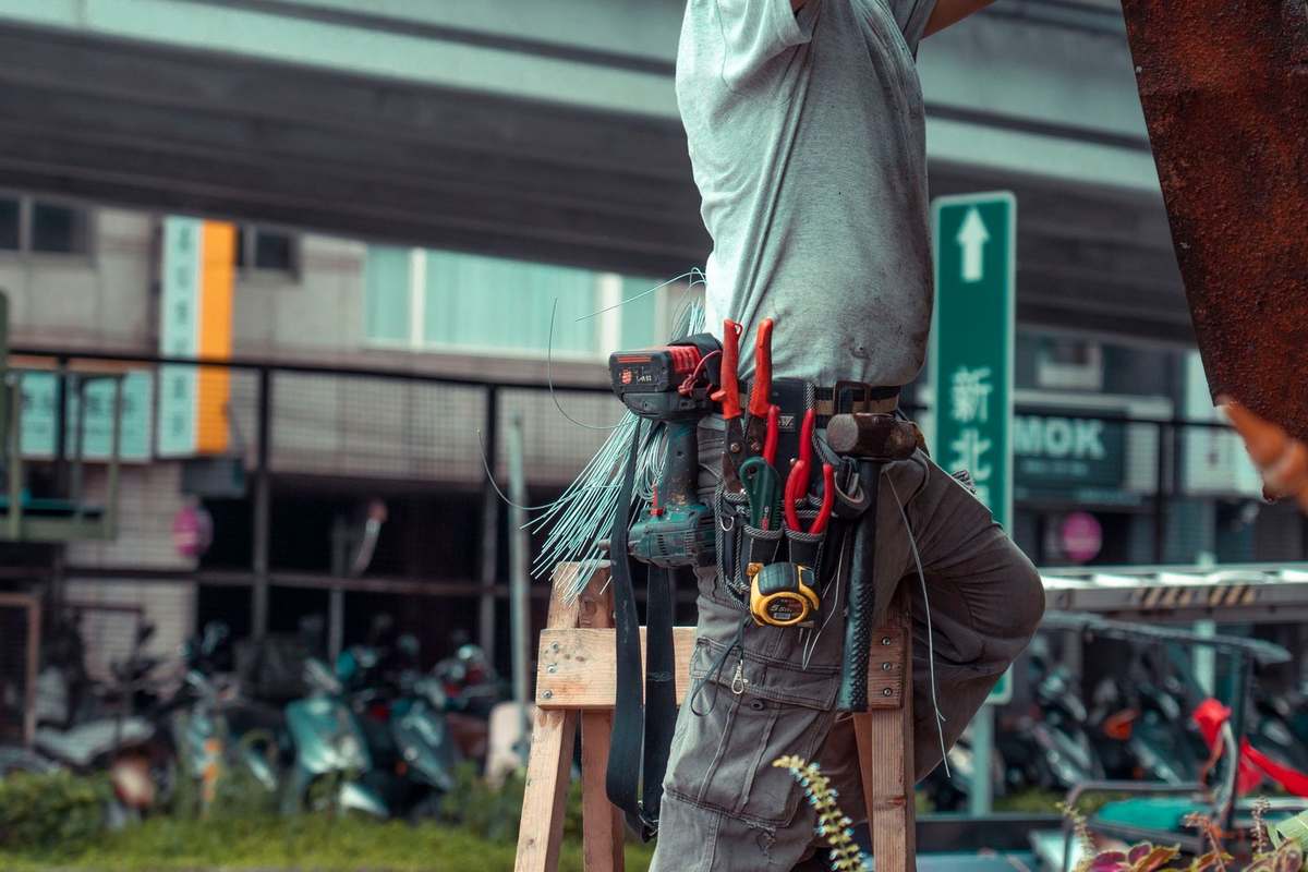 Homme en gris sur échelle avec outils, ville en arrière-plan Homme en gris sur échelle avec outils, ville en arrière-plan