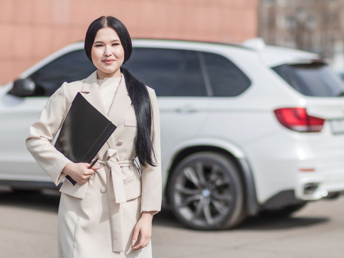 Femme asiatique en costume blanc portant un classeur devant une SUV blanche Femme asiatique en costume blanc portant un classeur devant une SUV blanche
